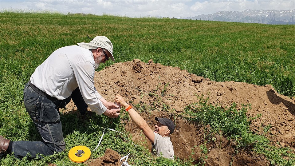 One man standing in a whole in the ground passing soil samples to another man. Photo: Miriam Meister